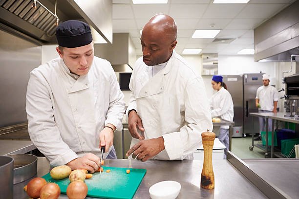 Teacher Helping Students Training To Work In Catering Chopping Vegetables